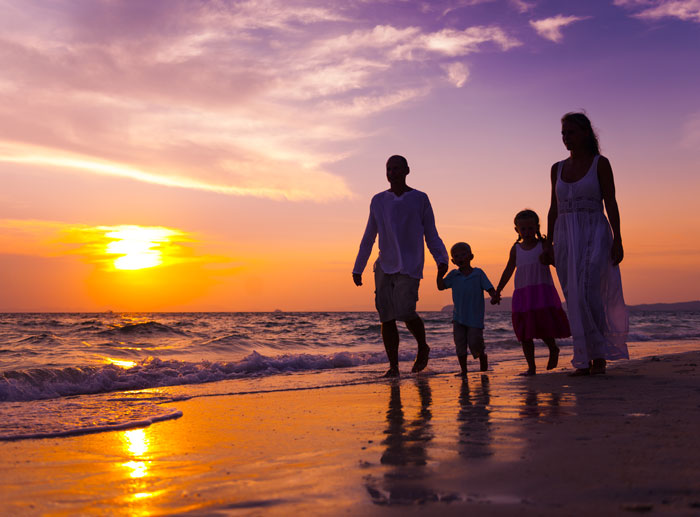 A family walks along a beach at sunset and enjoys their family friendly beach vacation.